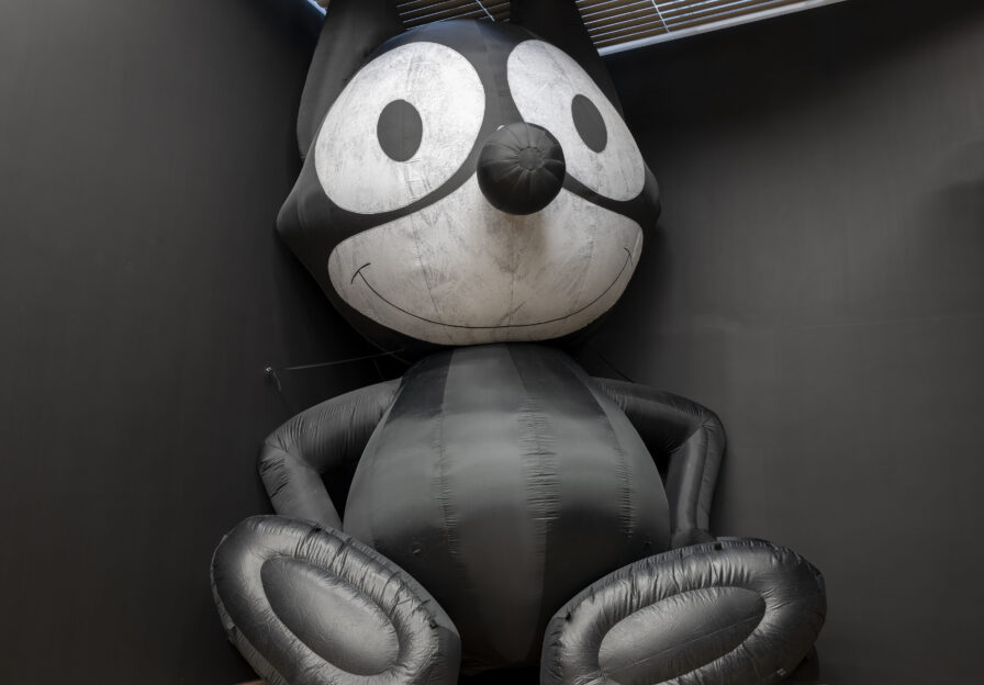 Ausstellungsansicht mit aufgeblasener Plastikkatze in der Ecke