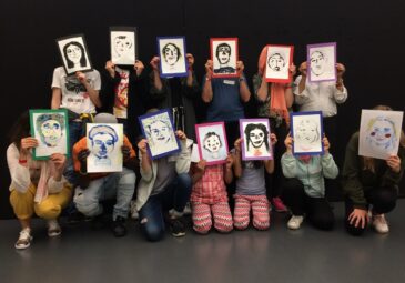 Foto einer Workshopgruppe mit gedruckten und farbig gestalteten Selbstporträts.
