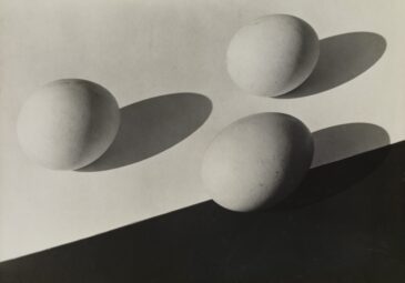 Schwarzweißfotografie von 3 Eiern auf Tisch mit langen Schlagschatten.