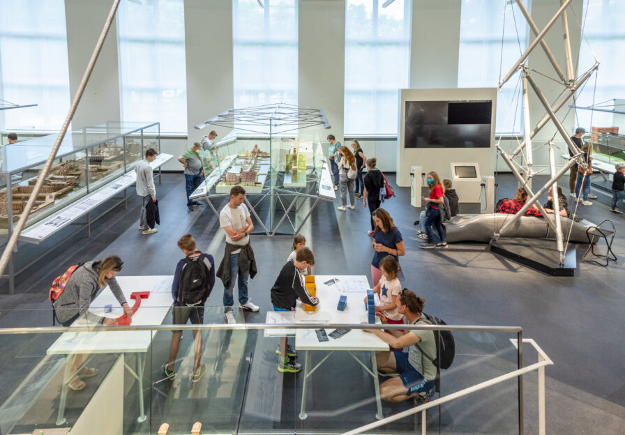 Blick in die Ausstellung mit den Bauklotz-Stationen im Vordergrund, dem Tensegrity-Turm rechts und Vitrinen mit Brückenmodellen.