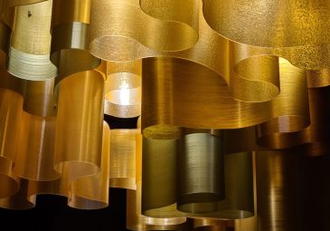 Goldfarbene Deckenleuchte aus geschwungenen Kieselalgenbahnen.