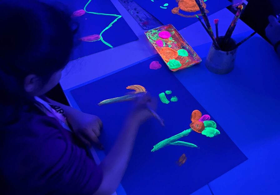 Kind malt auf Papier mit leuchtenden Farben bei Schwarzlicht
