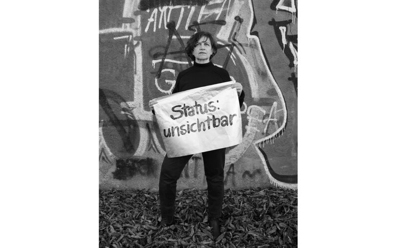Frau hält ein weißes Banner vor dem Körper mit der Aufschrift: "Status: unsichtbar".