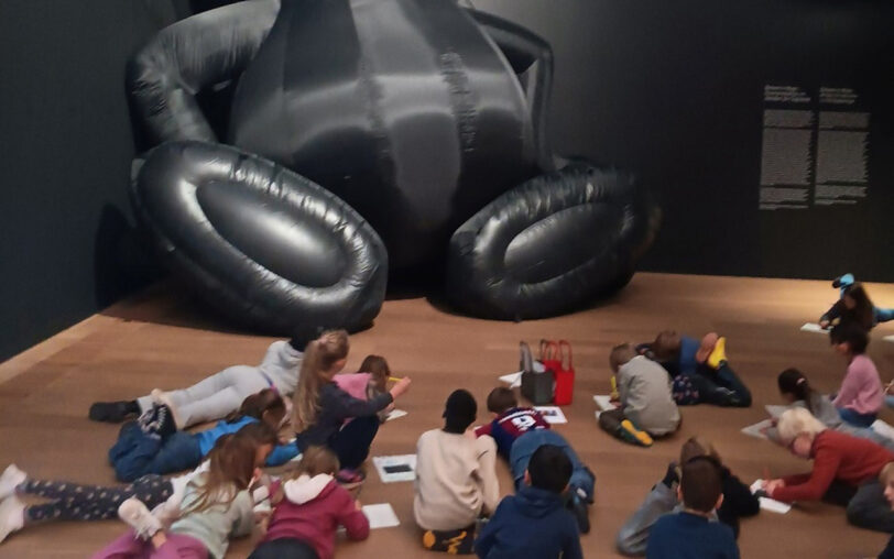 Eine Schulklasse sitzt verstreut am Boden vor einem riesigen Exponat im Museum Brandhorst.