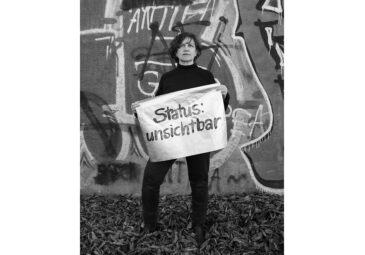 Frau hält ein weißes Banner vor dem Körper mit der Aufschrift: "Status: unsichtbar".