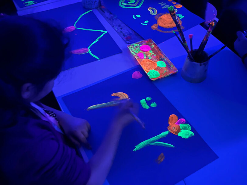 Zeichnen mit leuchtenden Farben in Raum mit Schwarzlicht.