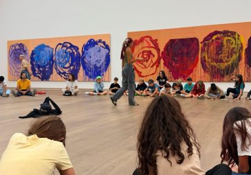 Eine Gruppe Schüler*innen sitzt im Kreis auf dem Boden in einem Ausstellungsraum
